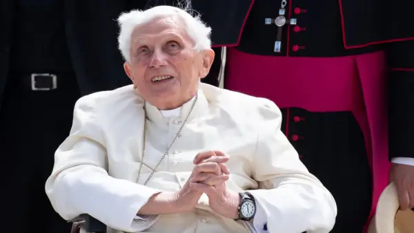 Emeritierter Papst Benedikt XVI. in weißer Soutane, Hände gefaltet, blickt lächelnd nach oben.
