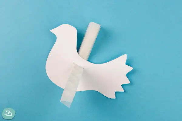 Eine weiße Papier-Friedenstaube wird mit Klebeband befestigt. Bastelanleitung für eine Friedenstaube.